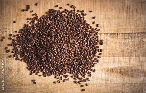 Roasted brown coffee beans spilled on wooden table background.