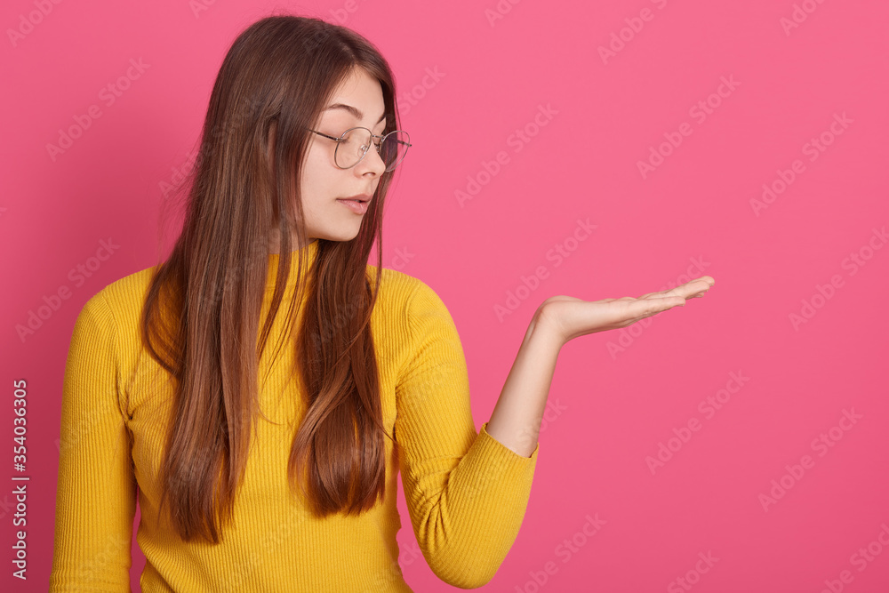 Profile of pensive dreamy attractive serious young girl looking aside, raising one hand, wearing spectacles and yellow sweatshirt, having long hair, being peaceful. Copyspace for advertisement.