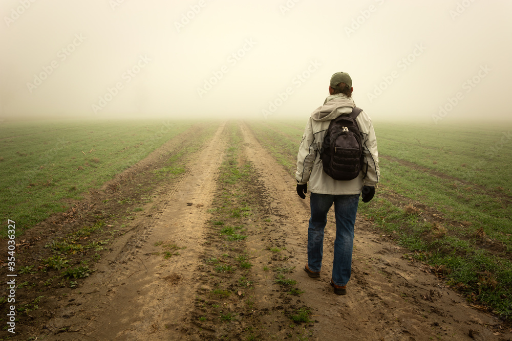 A man with a backpack walking towards the fog