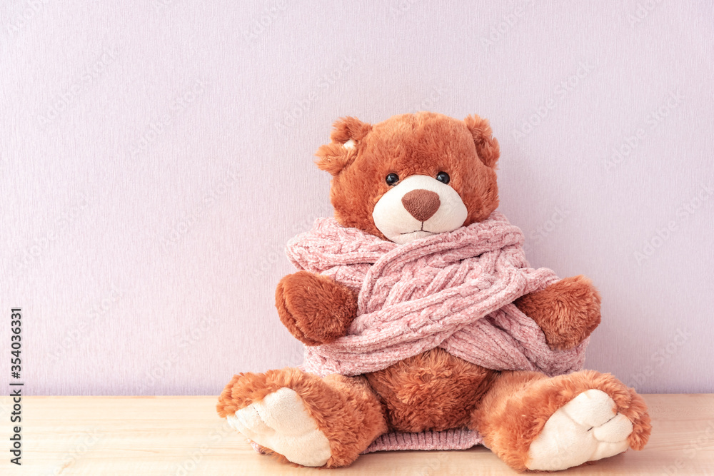 Cute toy teddy bear in pink knitted sweater sitting on shelf at home. Warm and cozy winter
