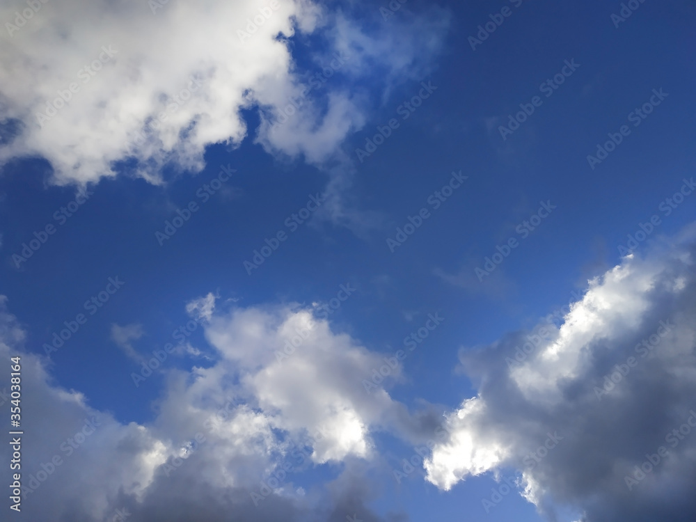 White and gray fluffy clouds illuminated by the sun on a blue sky background White and gray fluffy clouds illuminated by the sun on a blue sky background