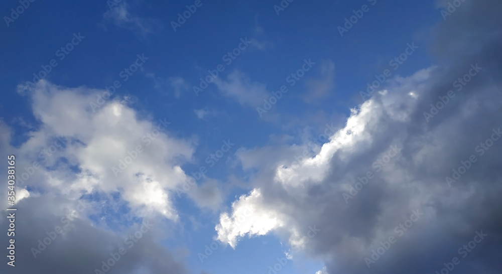 White and gray clouds illuminated by the sun on a blue sky background