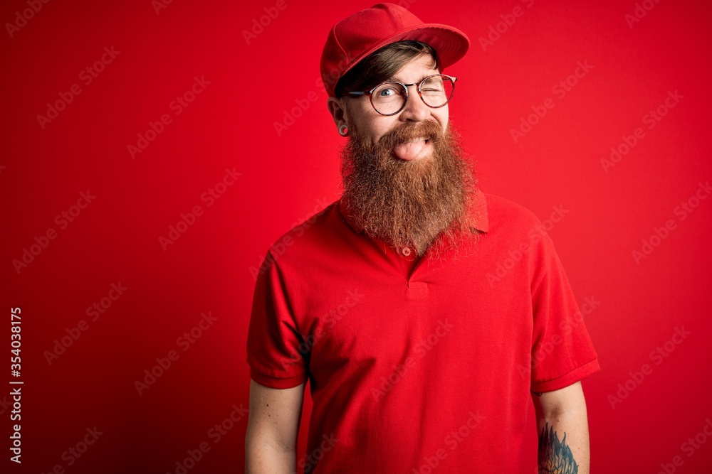 Young handsome delivery man wearing glasses and red cap over isolated background winking looking at the camera with sexy expression, cheerful and happy face.