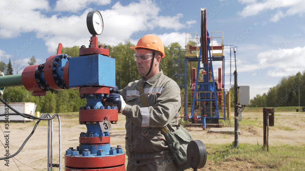 Φωτογραφία Oilman in orange helmet and protective glass closing valve of x-mass wellhead to shut off well