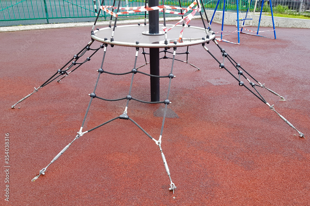 A children's sports complex on the playground wrapped with red barrier tape. Outdoors. Prohibition of outdoor walks, prevention of the biological hazard of the coronavirus influenza virus covid-19.