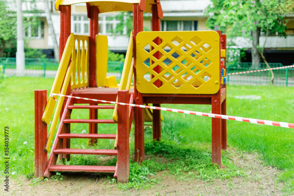 A yellow slide for children's park is wrapped with red barrier tape. Prohibition of outdoor walks, prevention of the biological hazard of the coronavirus influenza covid-19. caution. selective focus A yellow slide for children's park is wrapped with red barrier tape. Prohibition of outdoor walks, prevention of the biological hazard of the coronavirus influenza covid-19. caution. selective focus