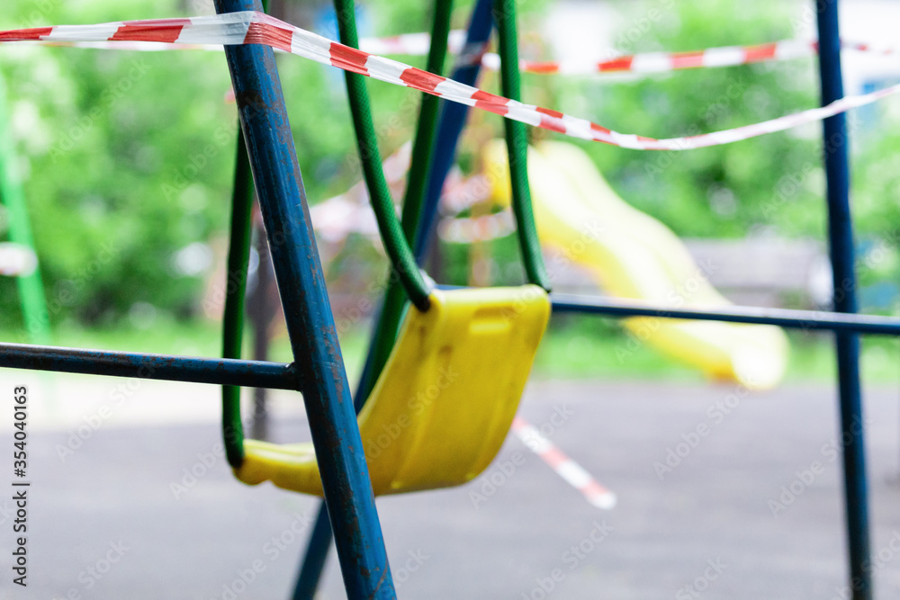 Yellow children's swing in the park wrapped with red barrier tape. Outside. Prohibition of outdoor walks, prevention of the coronavirus influenza virus covid-19. park closed. selective focus