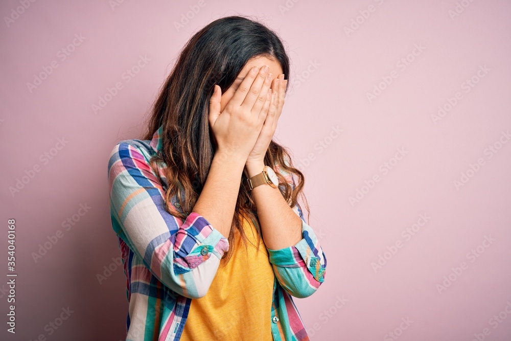 Young beautiful brunette woman wearing casual colorful shirt standing over pink background with sad expression covering face with hands while crying. Depression concept. Young beautiful brunette woman wearing casual colorful shirt standing over pink background with sad expression covering face with hands while crying. Depression concept.