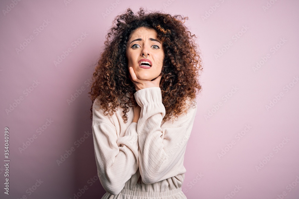 Beautiful woman with curly hair and piercing wearing casual sweater over pink background shouting and suffocate because painful strangle. Health problem. Asphyxiate and suicide concept. Beautiful woman with curly hair and piercing wearing casual sweater over pink background shouting and suffocate because painful strangle. Health problem. Asphyxiate and suicide concept.