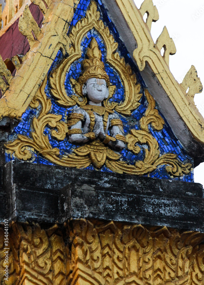 Golden fresco of a buddha image on a blue glass mosaic design on a gable of a wat or buddhist temple in Siamese Lao PDR, Southeast Asia