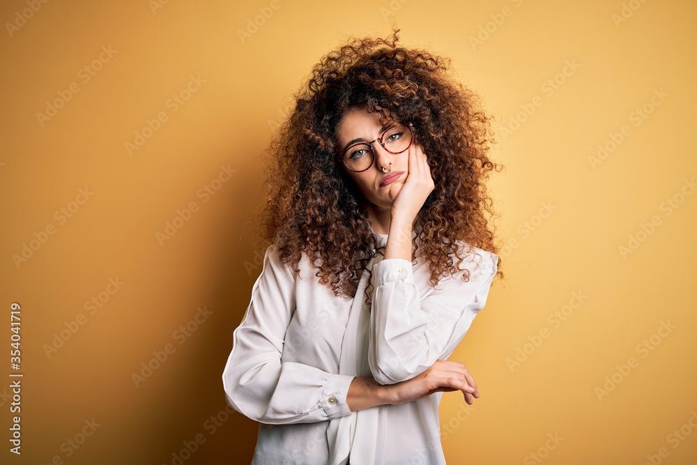 Young beautiful brunette woman with curly hair and piercing wearing shirt and glasses thinking looking tired and bored with depression problems with crossed arms. Young beautiful brunette woman with curly hair and piercing wearing shirt and glasses thinking looking tired and bored with depression problems with crossed arms.