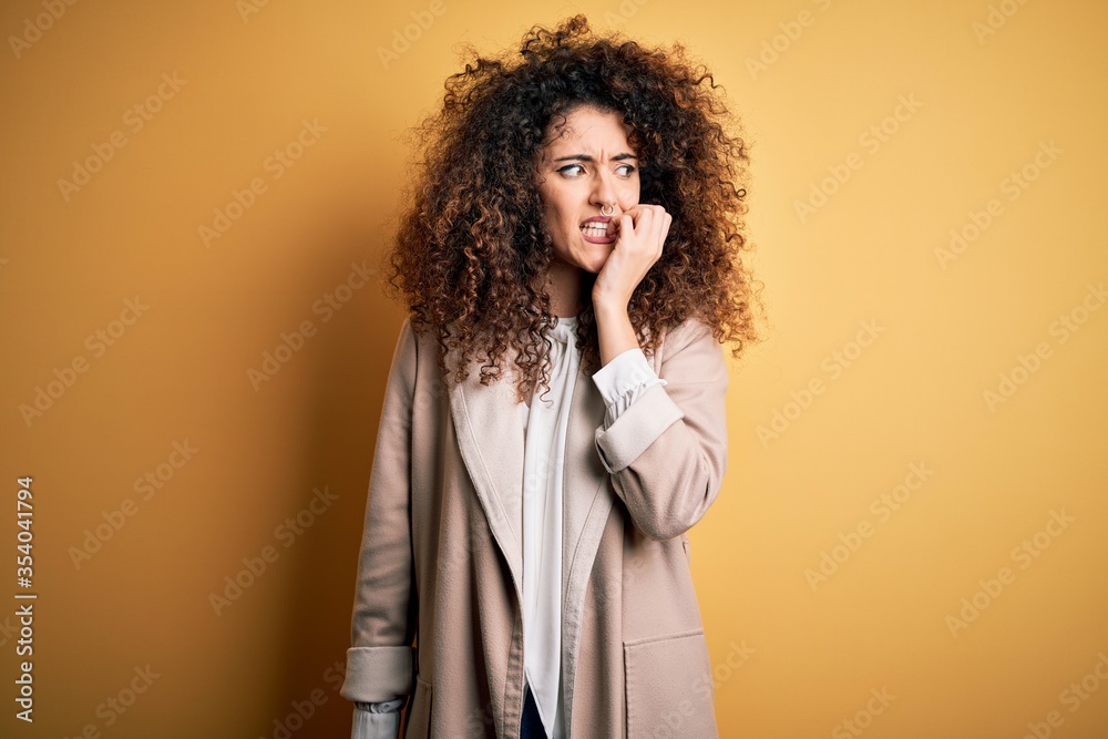 Young beautiful brunette woman with curly hair and piercing wearing casual t-shirt and diadem looking stressed and nervous with hands on mouth biting nails. Anxiety problem. Young beautiful brunette woman with curly hair and piercing wearing casual t-shirt and diadem looking stressed and nervous with hands on mouth biting nails. Anxiety problem.