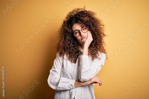 Young beautiful brunette woman with curly hair and piercing wearing shirt and glasses thinking looking tired and bored with depression problems with crossed arms. © Krakenimages.com