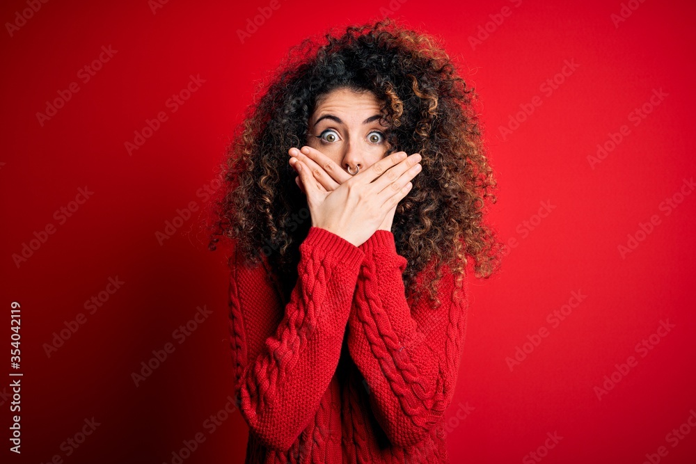 Young beautiful woman with curly hair and piercing wearing casual red sweater shocked covering mouth with hands for mistake. Secret concept. Young beautiful woman with curly hair and piercing wearing casual red sweater shocked covering mouth with hands for mistake. Secret concept.