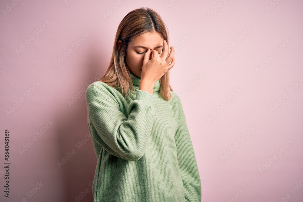 Young beautiful blonde woman wearing winter wool sweater over pink isolated background tired rubbing nose and eyes feeling fatigue and headache. Stress and frustration concept. Young beautiful blonde woman wearing winter wool sweater over pink isolated background tired rubbing nose and eyes feeling fatigue and headache. Stress and frustration concept.