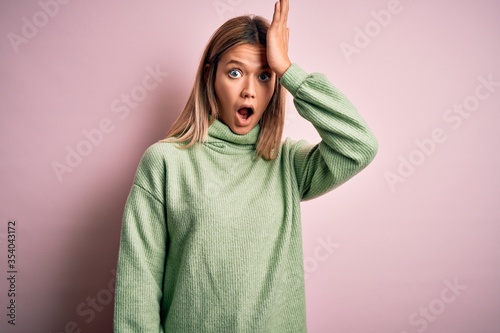 Young beautiful blonde woman wearing winter wool sweater over pink isolated background surprised with hand on head for mistake, remember error. Forgot, bad memory concept. © Krakenimages.com
