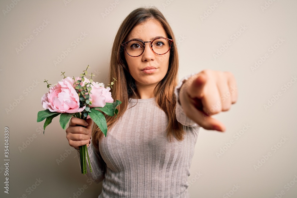 Young blonde woman holding beautiful romantic floral bouquet over isolated background pointing with finger to the camera and to you, hand sign, positive and confident gesture from the front Young blonde woman holding beautiful romantic floral bouquet over isolated background pointing with finger to the camera and to you, hand sign, positive and confident gesture from the front