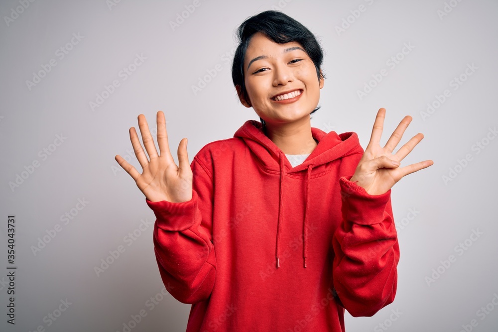 Young beautiful asian girl wearing casual sweatshirt with hoodie over white background showing and pointing up with fingers number nine while smiling confident and happy. Young beautiful asian girl wearing casual sweatshirt with hoodie over white background showing and pointing up with fingers number nine while smiling confident and happy.