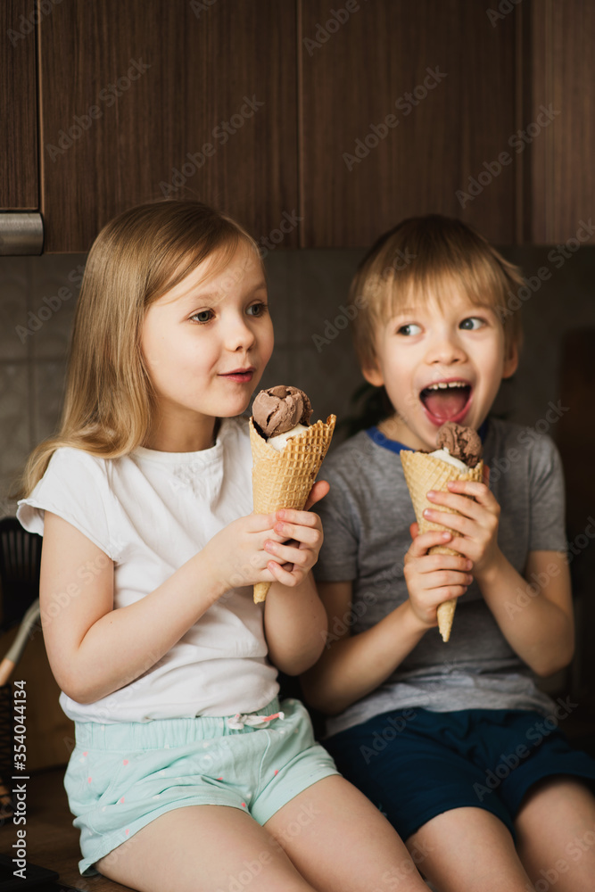 Two little kids eating ice cream in kitchen at home Two little kids eating ice cream in kitchen at home