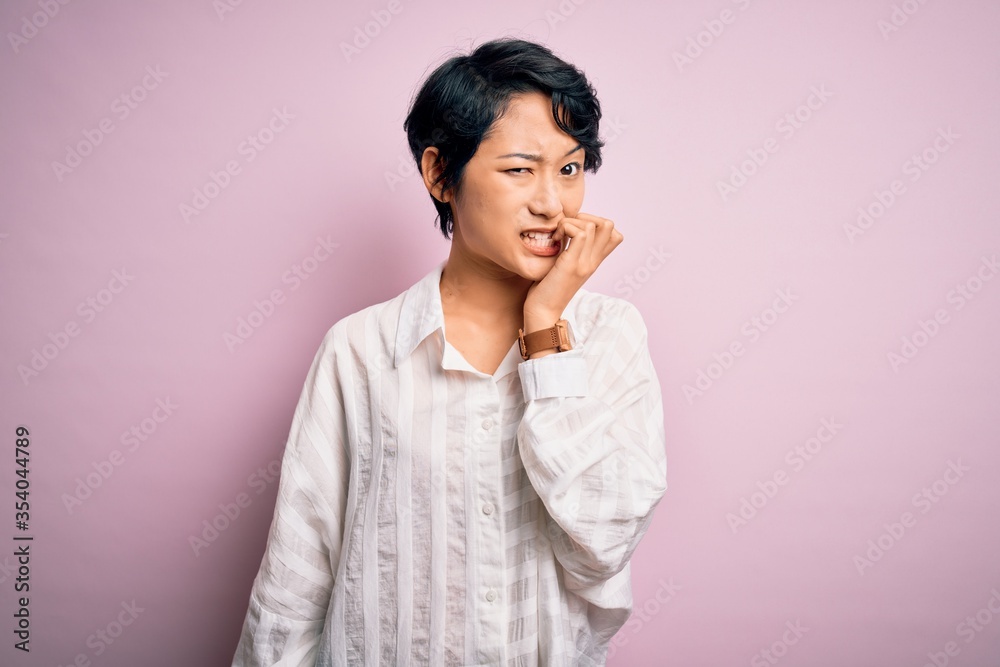 Young beautiful asian girl wearing casual shirt standing over isolated pink background looking stressed and nervous with hands on mouth biting nails. Anxiety problem. Young beautiful asian girl wearing casual shirt standing over isolated pink background looking stressed and nervous with hands on mouth biting nails. Anxiety problem.