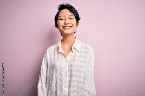 Young beautiful asian girl wearing casual shirt standing over isolated pink background with a happy and cool smile on face. Lucky person.
