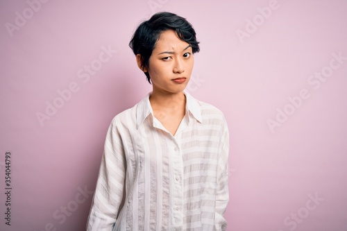 Young beautiful asian girl wearing casual shirt standing over isolated pink background skeptic and nervous, frowning upset because of problem. Negative person.