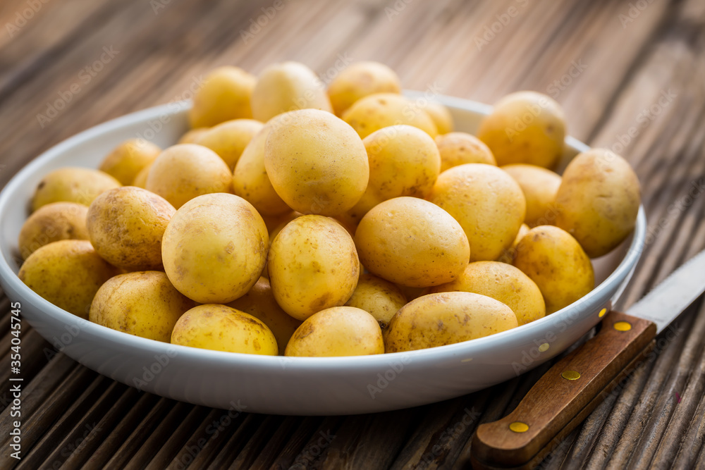 Fresh organic small potatoes in bowl with knife on wooden background Fresh organic small potatoes in bowl with knife on wooden background