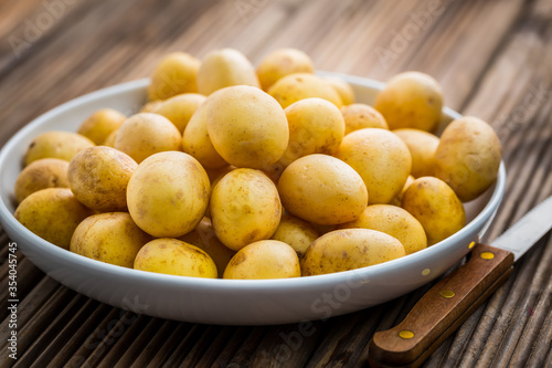 Fresh organic small potatoes in bowl with knife on wooden background