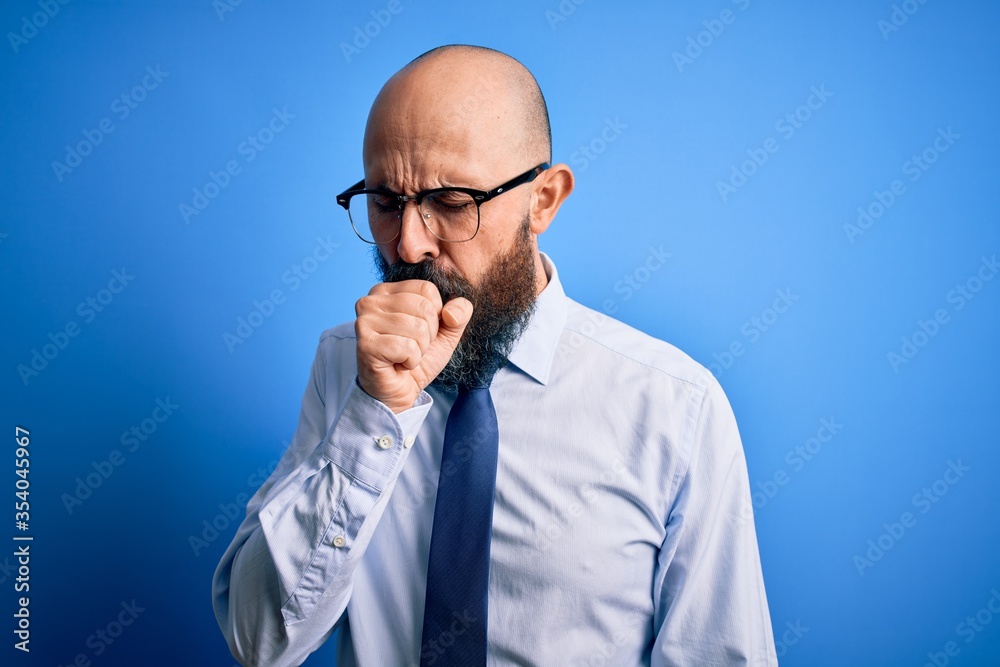 Handsome business bald man with beard wearing elegant tie and glasses over blue background feeling unwell and coughing as symptom for cold or bronchitis. Health care concept. Handsome business bald man with beard wearing elegant tie and glasses over blue background feeling unwell and coughing as symptom for cold or bronchitis. Health care concept.