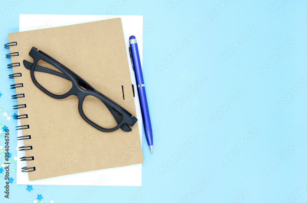 Father's day greeting card. Craft notebook, white sheet with a pen on a blue background. Black-rimmed glasses. Copyspace with space for your text. The view from the top. Flatly.