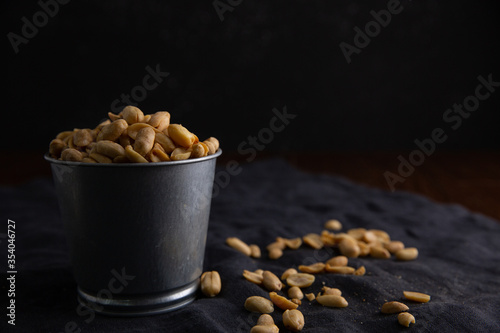 A pile of peanuts in a zinc cup on a black top