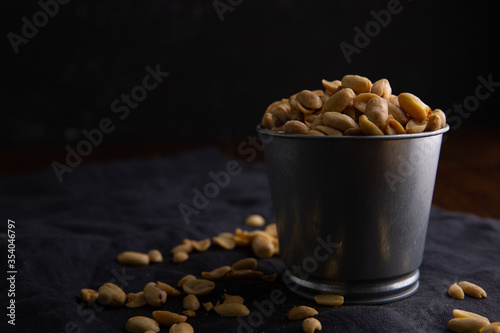 A pile of peanuts in a zinc cup on a black top