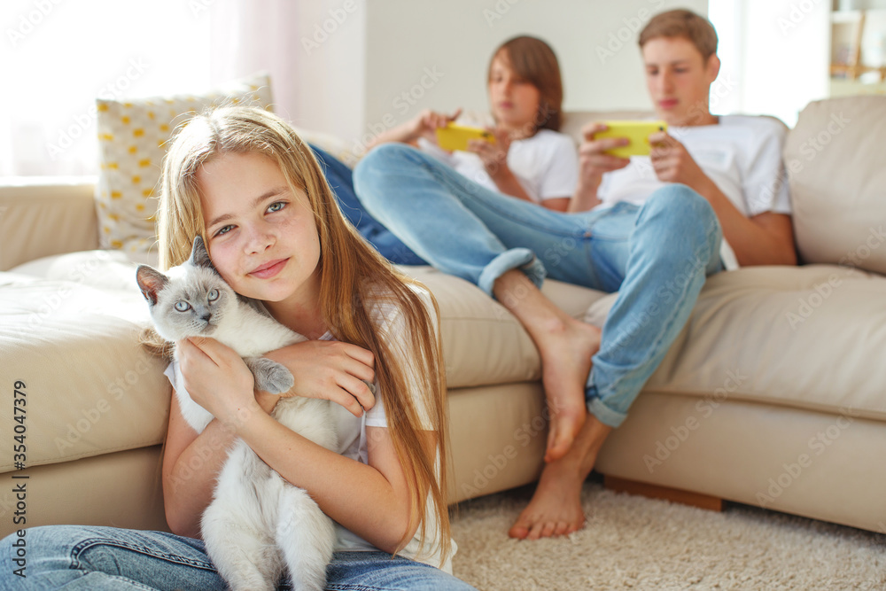 Children play different games. The girl holds a cat in her arms, and the boys play on the phones.