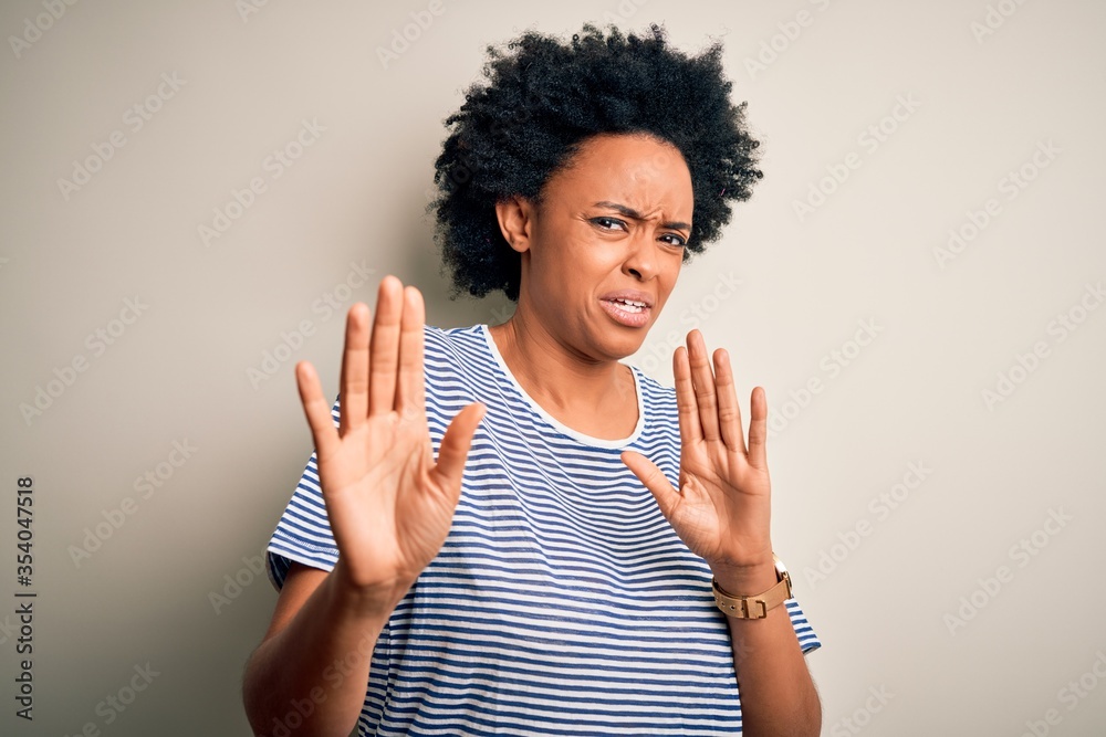 Young beautiful African American afro woman with curly hair wearing striped t-shirt disgusted expression, displeased and fearful doing disgust face because aversion reaction. With hands raised Young beautiful African American afro woman with curly hair wearing striped t-shirt disgusted expression, displeased and fearful doing disgust face because aversion reaction. With hands raised