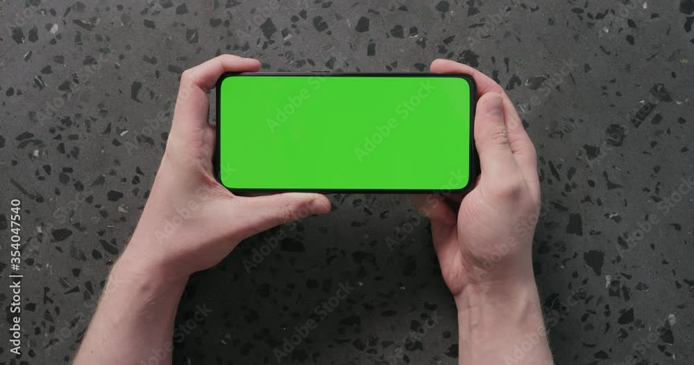 Top view man hands watch something on smartphone with green screen on concrete background Top view man hands watch something on smartphone with green screen on concrete background