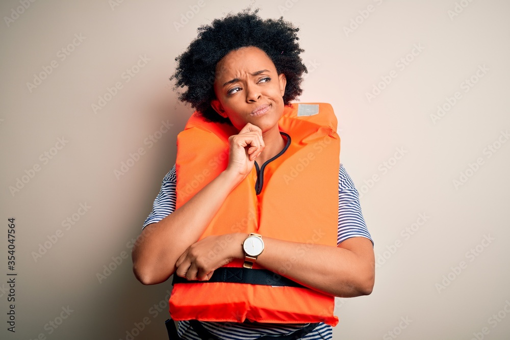 Young African American afro woman with curly hair wearing orange protection lifejacket with hand on chin thinking about question, pensive expression. Smiling with thoughtful face. Doubt concept. Young African American afro woman with curly hair wearing orange protection lifejacket with hand on chin thinking about question, pensive expression. Smiling with thoughtful face. Doubt concept.