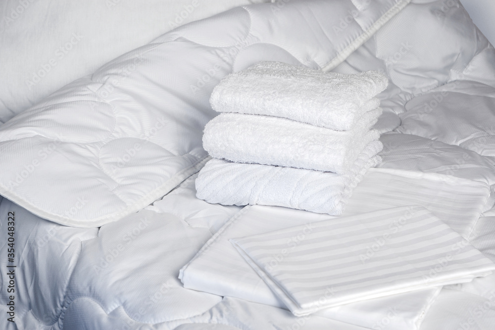 Towels are on bed. White bedding close-up. Clean terry towels on bedstead. Concept - bed linen at hotel. Sewing industry. Several towels lie on in a pile. Sale of sets with bed linen. Textile - obrazy, fototapety, plakaty 