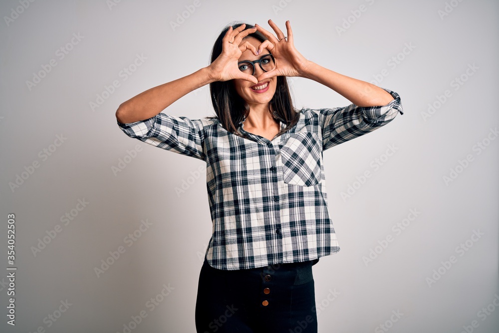 Young brunette woman with blue eyes wearing casual shirt and glasses over white background Doing heart shape with hand and fingers smiling looking through sign Young brunette woman with blue eyes wearing casual shirt and glasses over white background Doing heart shape with hand and fingers smiling looking through sign