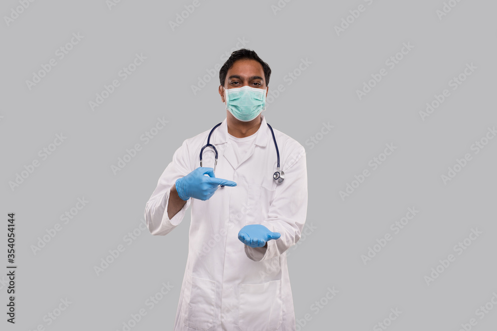 Doctor Pointing at Empty Open Hand in front of Chest Wearing Medical Mask and Gloves Isolated. Indian Man Doctor Advertisment Concept Doctor Pointing at Empty Open Hand in front of Chest Wearing Medical Mask and Gloves Isolated. Indian Man Doctor Advertisment Concept
