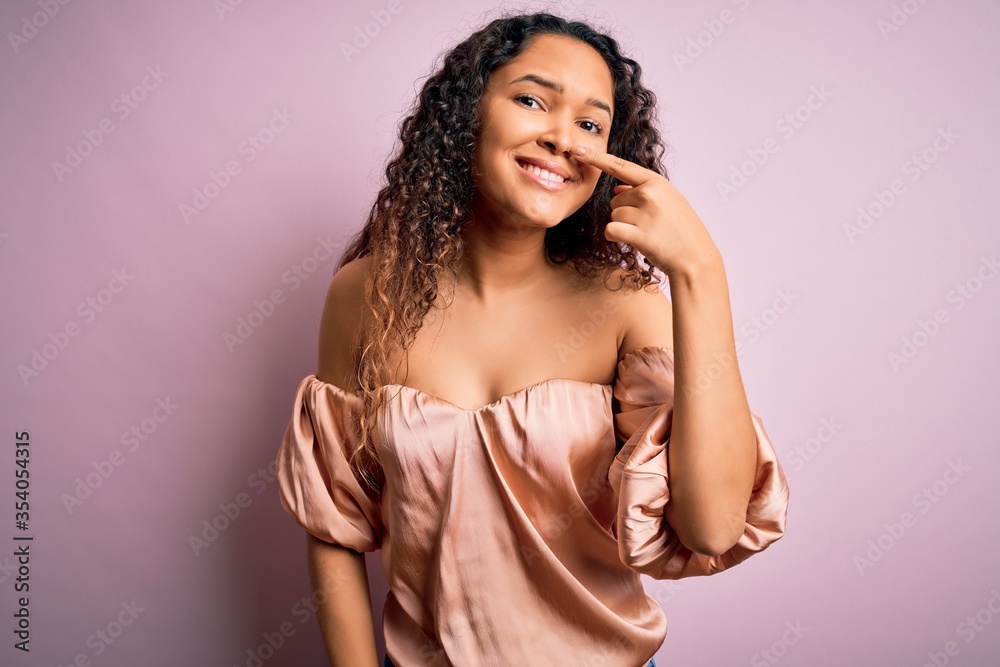 Young beautiful woman with curly hair wearing casual t-shirt standing over pink background Pointing with hand finger to face and nose, smiling cheerful. Beauty concept Young beautiful woman with curly hair wearing casual t-shirt standing over pink background Pointing with hand finger to face and nose, smiling cheerful. Beauty concept