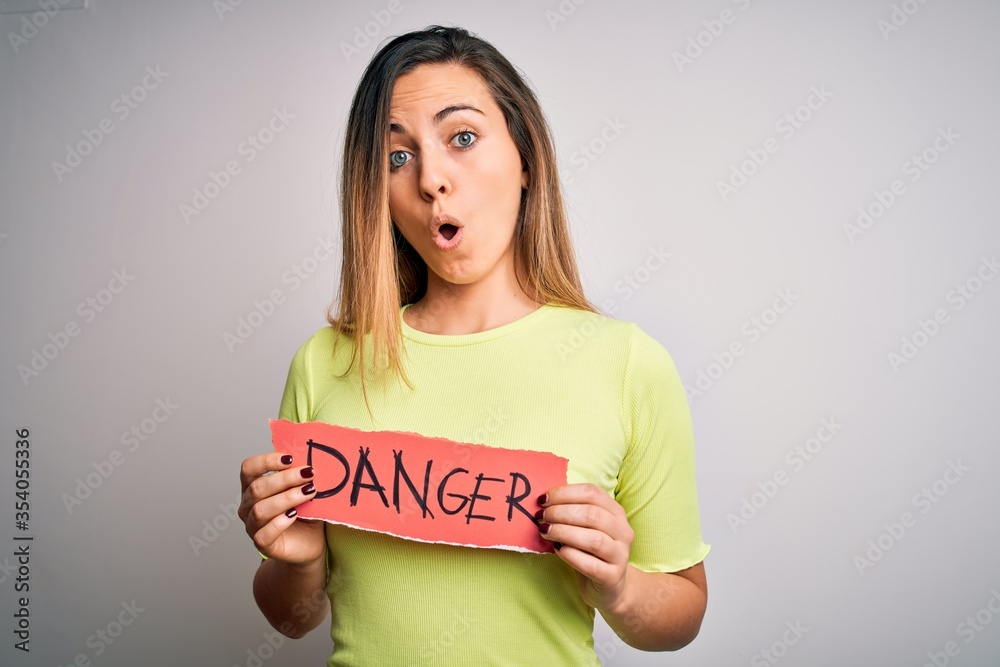 Young beautiful blonde woman with blue eyes holding paper with danger message scared in shock with a surprise face, afraid and excited with fear expression Young beautiful blonde woman with blue eyes holding paper with danger message scared in shock with a surprise face, afraid and excited with fear expression