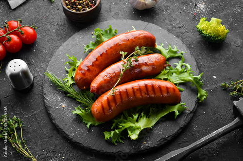 Smoked sausages with spices on a black stone plate. Top view. Old background, rustic style.