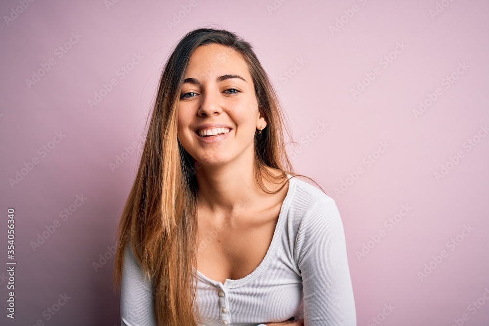 Young beautiful blonde woman with blue eyes wearing white t-shirt over pink background smiling and laughing hard out loud because funny crazy joke with hands on body. Young beautiful blonde woman with blue eyes wearing white t-shirt over pink background smiling and laughing hard out loud because funny crazy joke with hands on body.