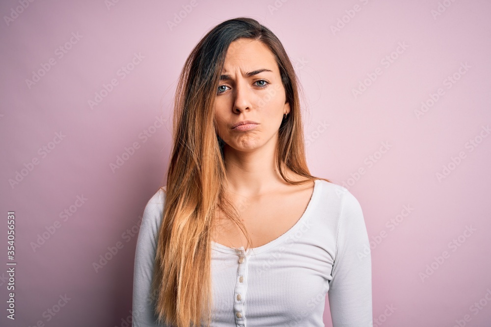 Fototapeta premium Young beautiful blonde woman with blue eyes wearing white t-shirt over pink background depressed and worry for distress, crying angry and afraid. Sad expression.