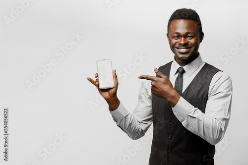 Black african business man points to his phone. Electronic store worker. Successful people lifestyle advert. You can win a prize in online bet. Man separete white background