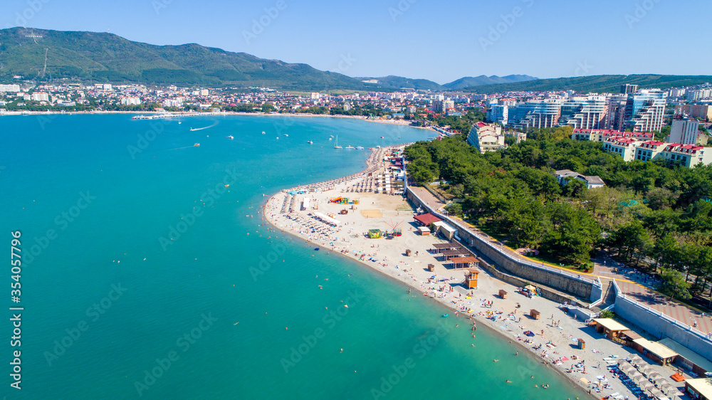 Beach of Gelendzhik resort. Numerous sun umbrellas and sun loungers. Embankment with balustrade. Houses and trees behind the embankment