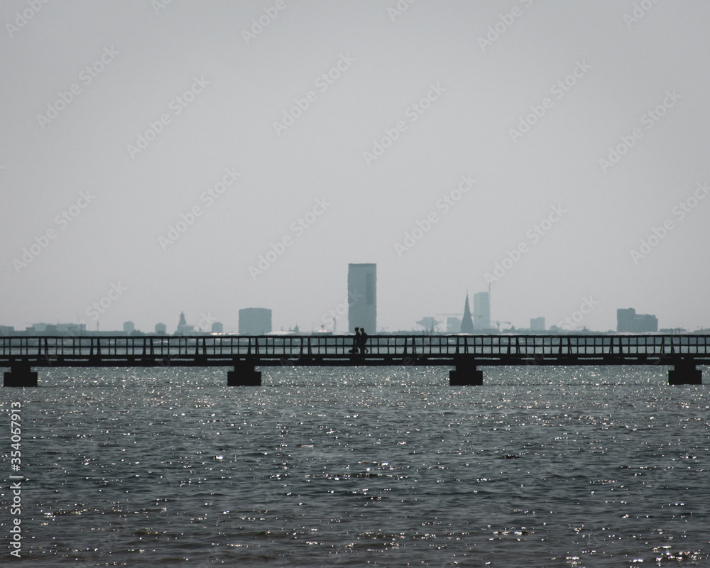 Walking on bridge over ocean water with city in background