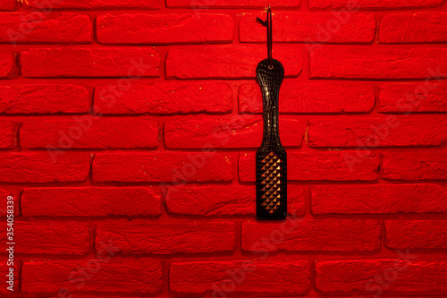 top view of black spanking paddle on red brick wall