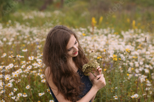 Young beautiful girl holds bouquet of flowers in hands in chamomile field