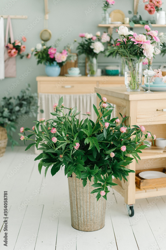 Peony flowers bouquet at the wooden kitchen island on the bright wooden handmade kitchen. Flowers in tall golden tin bucket.
